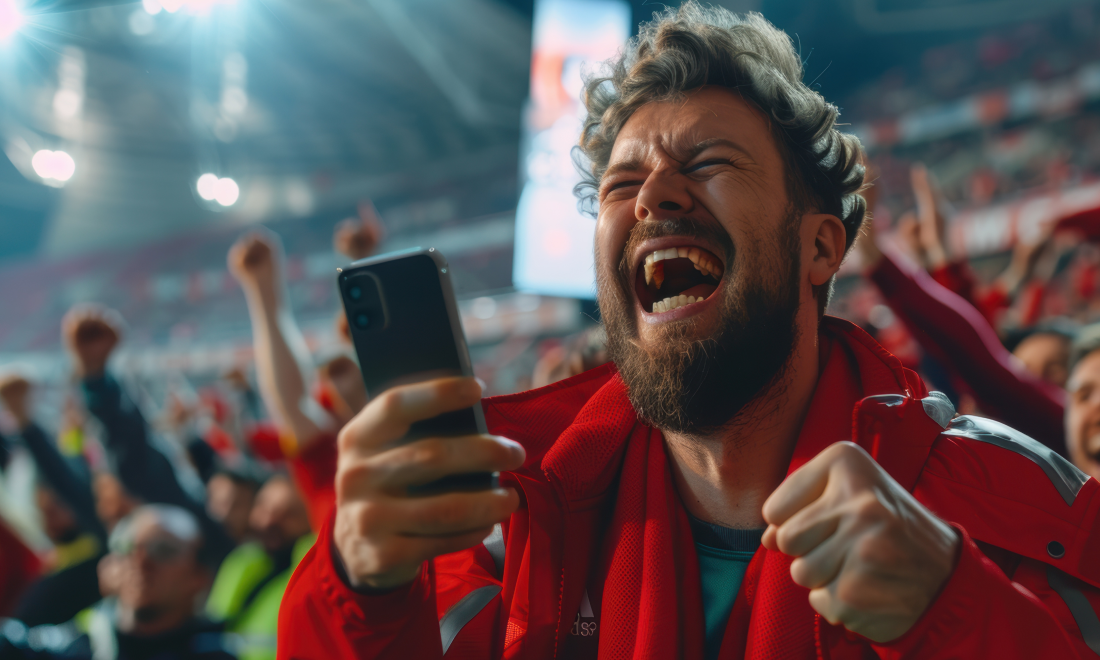 Mann på fotballkamp med telefon