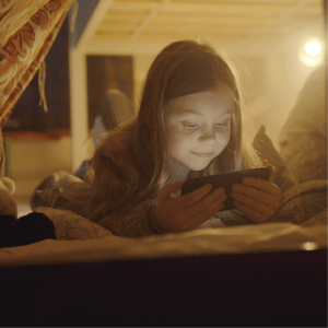 Jente som ligger og ser på mobilen sin med en nattlampe