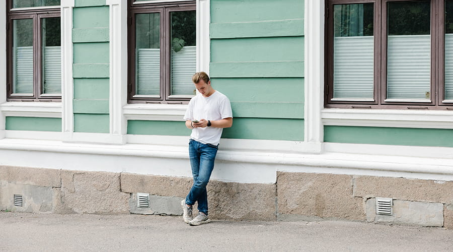 Bilde av mann som ser på tlf mens han lener seg mot vegg