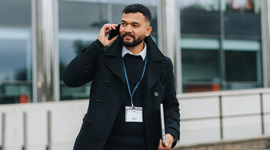 Mann snakker i telefon med ansattkort rundt halsen.