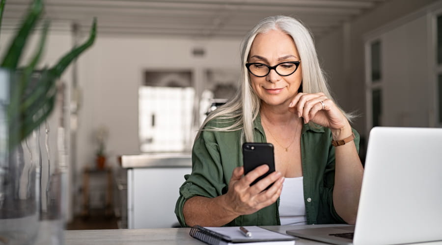 Dame sitter og ser på mobilen sin foran en PC og notatblokk