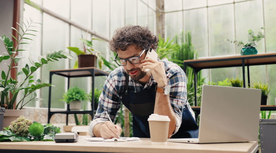 Mann sitter i en telefonsamtale mens han noterer ned ting på et papir som ligger på pulten sin. 