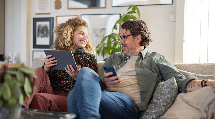 Far og datter i sofa med mobil og tablet