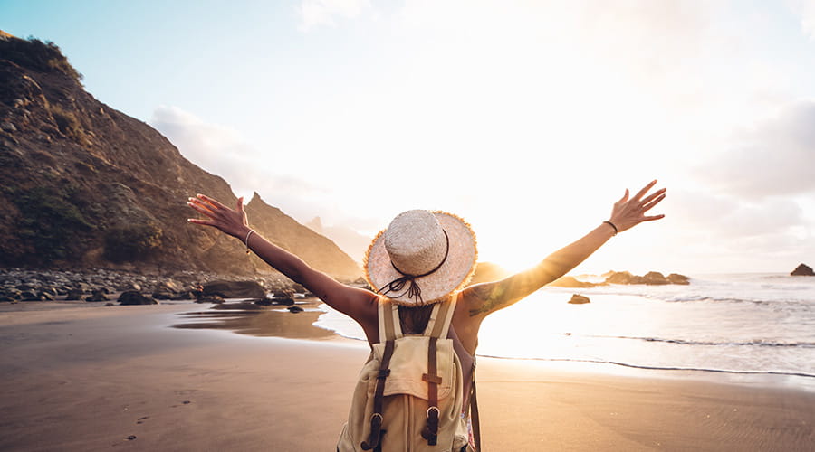 Dame som står på stranden med armene ut mot solnedgang