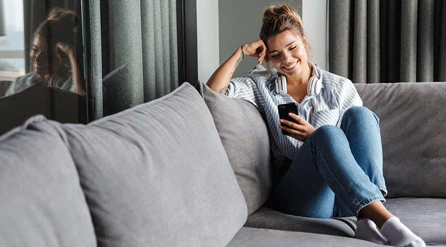 Dame som sitter i sofaen og ser på telefonen sin