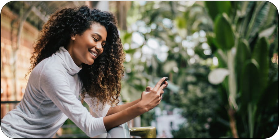 Dame som står i et drivhus fullt av planter som ser på mobilen og smiler