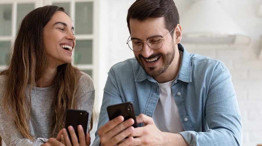 Mann og dame som ser på hver sin telefon og smiler