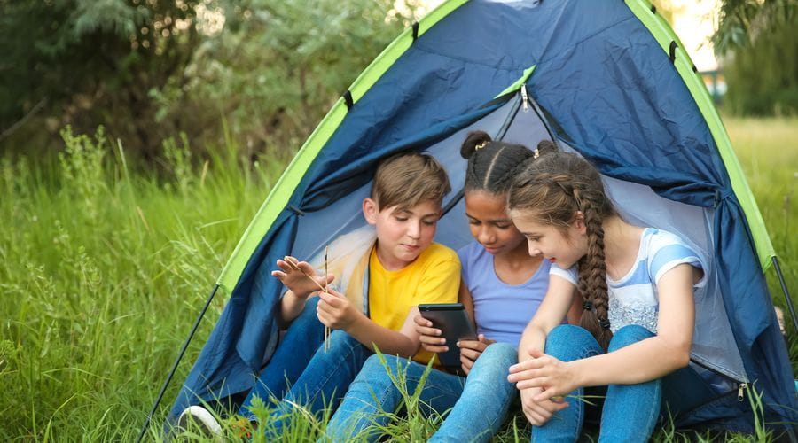 Barn som sitter i et telt ute mens de deler på en mobil