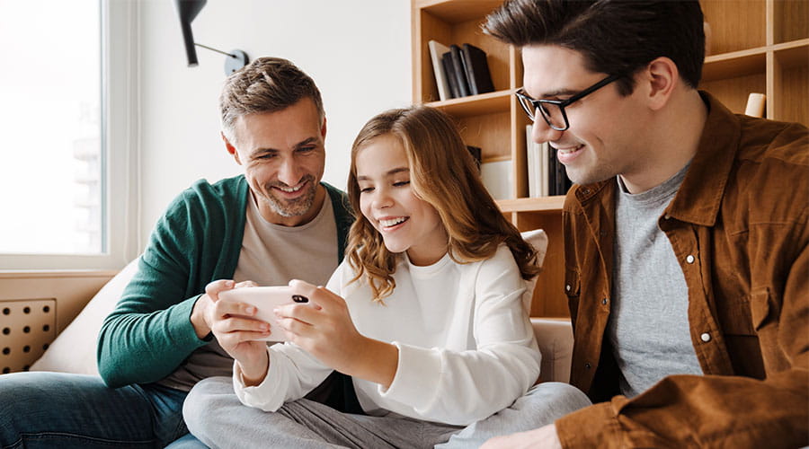 To voksne og en datter ser på noe gøy på en mobil sammen