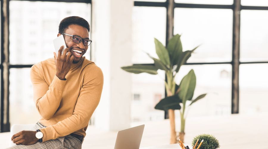 Mann i gul genser som ler mens han snakker i telefonen