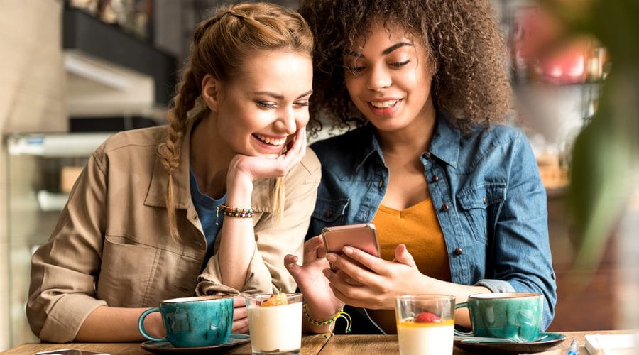 To jenter på cafe som ser på telefonen