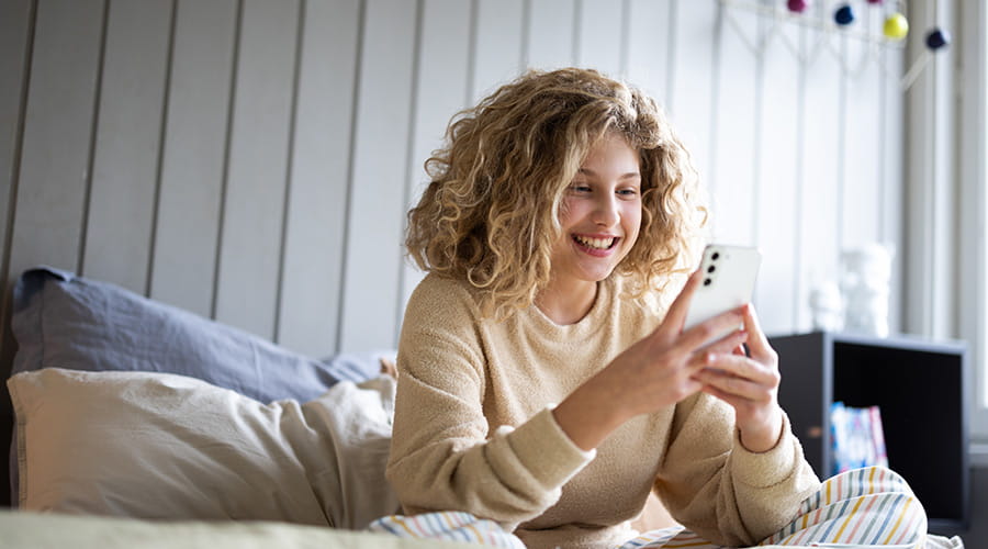 Jente som sitter i sengen å ser på telefonen sin