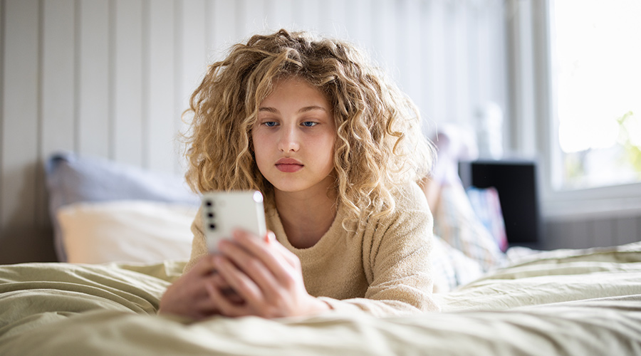 Jente som ligger på sengen å ser på telefonen