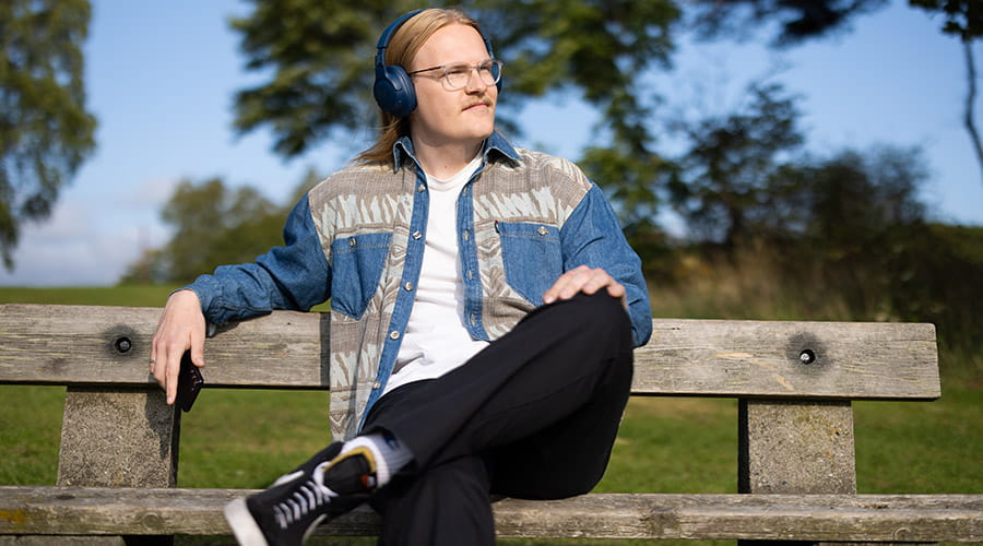 Gutt som sitter på en benk å hører på musikk