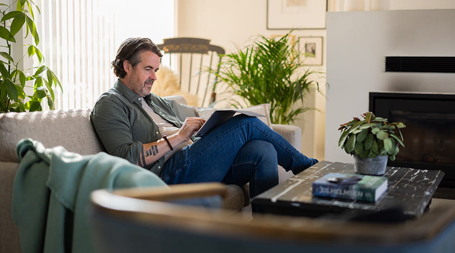 Mann som sitter i sofaen å ser på nettbrettet