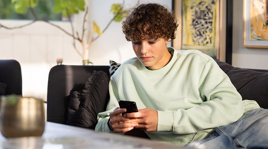 Gutt som ligger å ser på telefonen