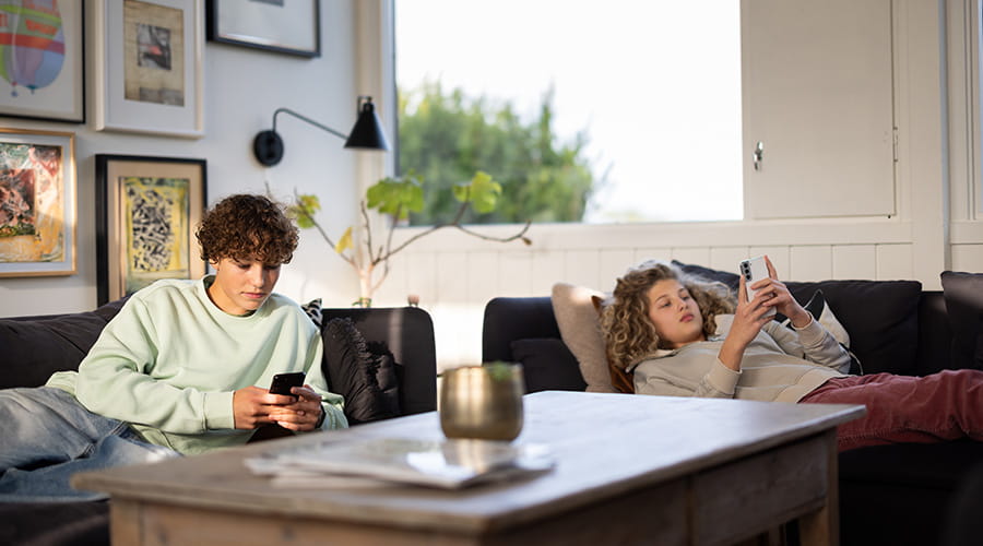 Søsken som ligger på hver sin sofa å ser på mobilen