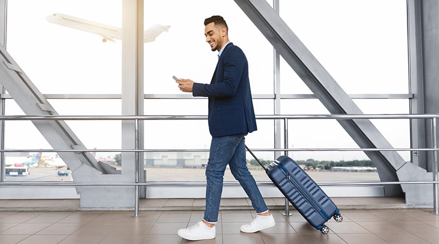 Bilde av en mann som går i en flyplass mens han ser på mobilen sin